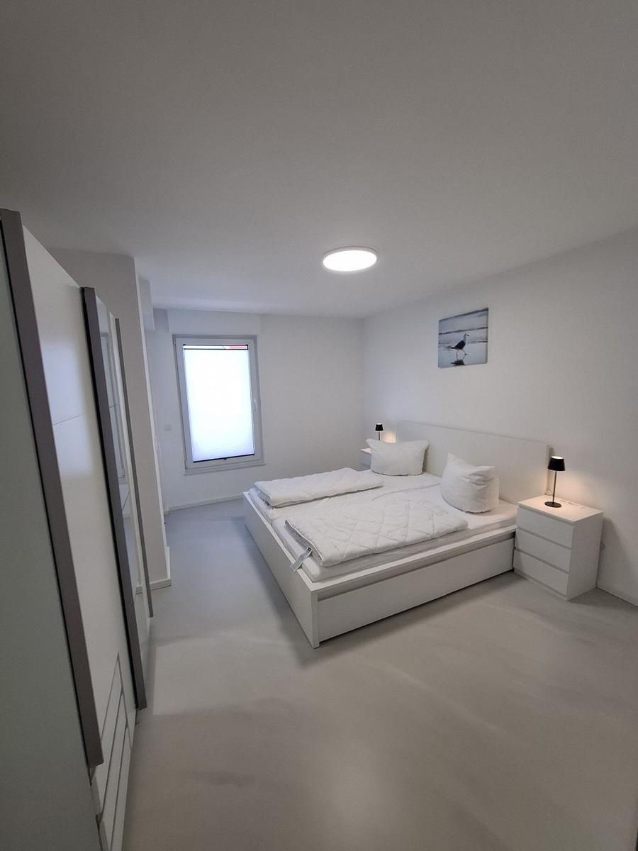 Schlafzimmer mit weißem Bett, Nachttischen und Fenster.