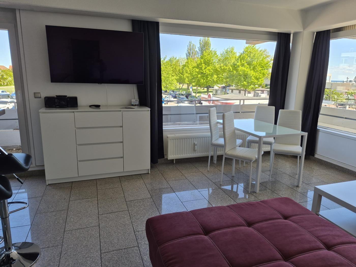 Wohnzimmer mit TV, Esstisch und Blick auf Grünflächen.