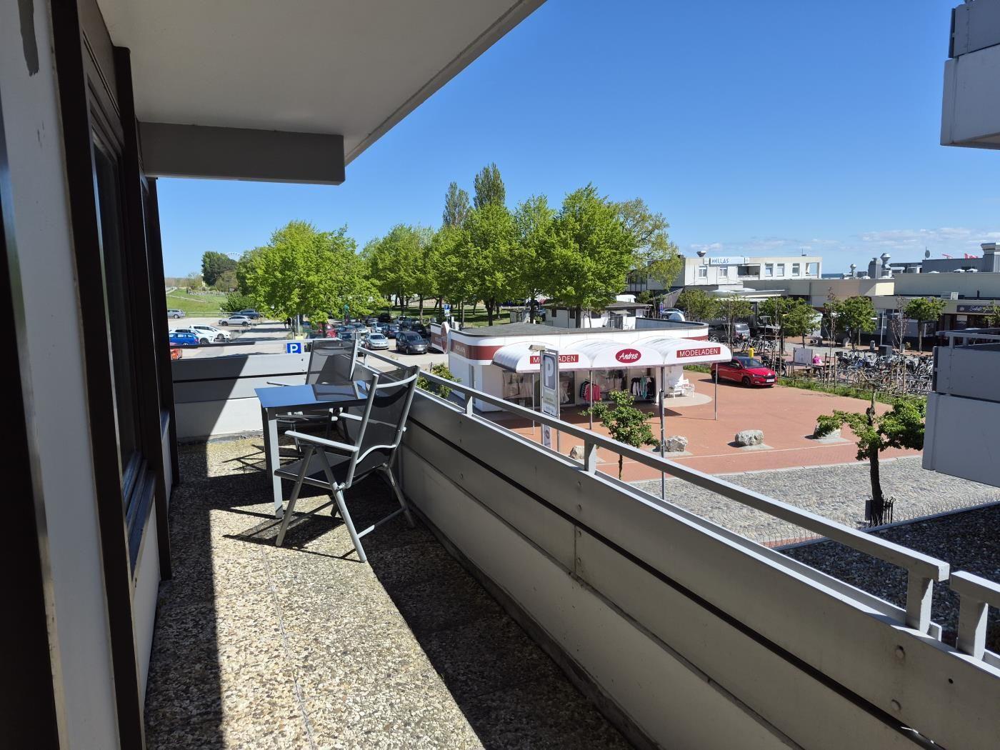 Terrasse mit Tisch und Stühlen. Blick auf Parkplatz und Geschäfte.