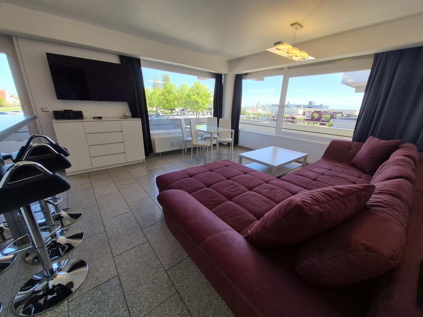 Wohnzimmer mit rotem Sofa, TV und großem Fensterblick.