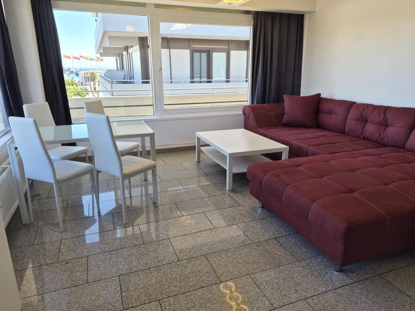 Wohn- und Essbereich mit rotem Sofa, weißem Tisch und großem Fenster mit Blick.