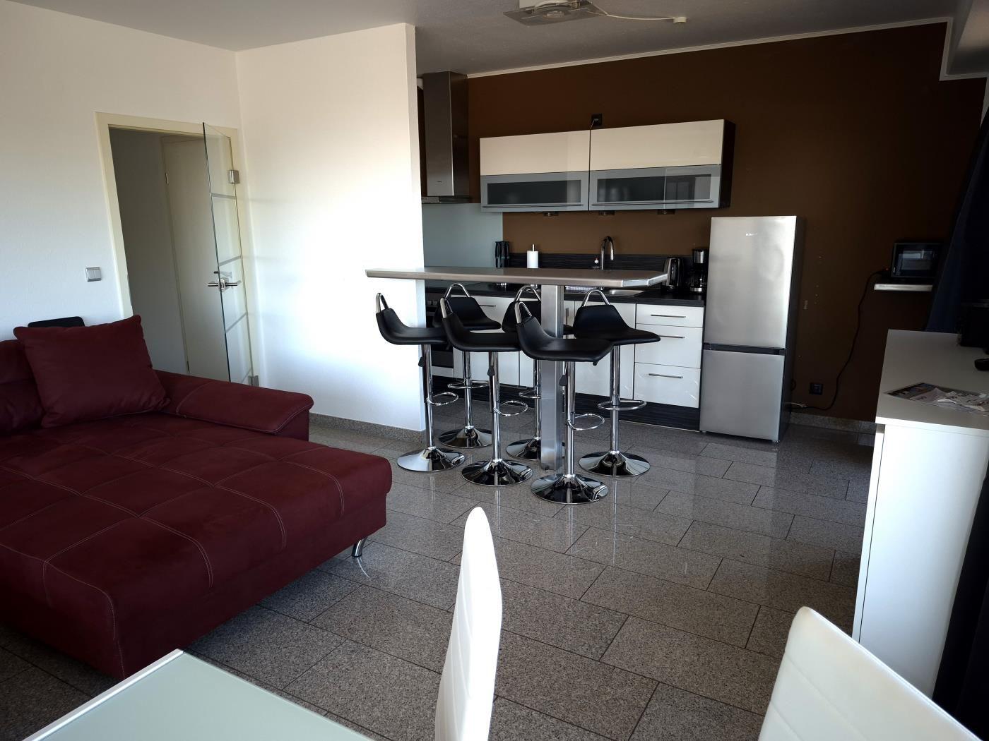 Wohnbereich mit rotem Sofa, Kücheninsel und Stühlen