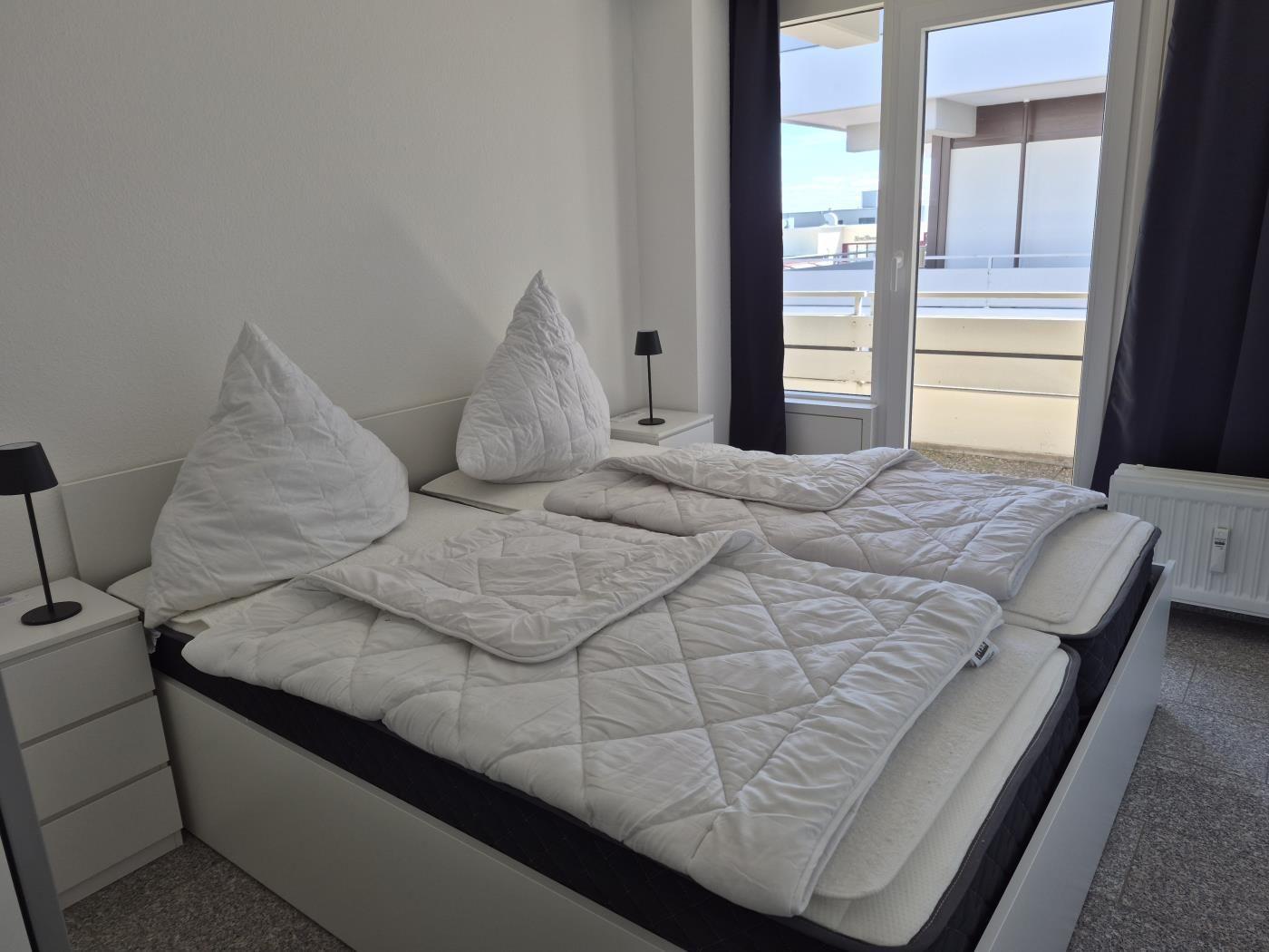 Schlafzimmer mit Doppelbett, zwei Nachttischen und Balkonansicht.