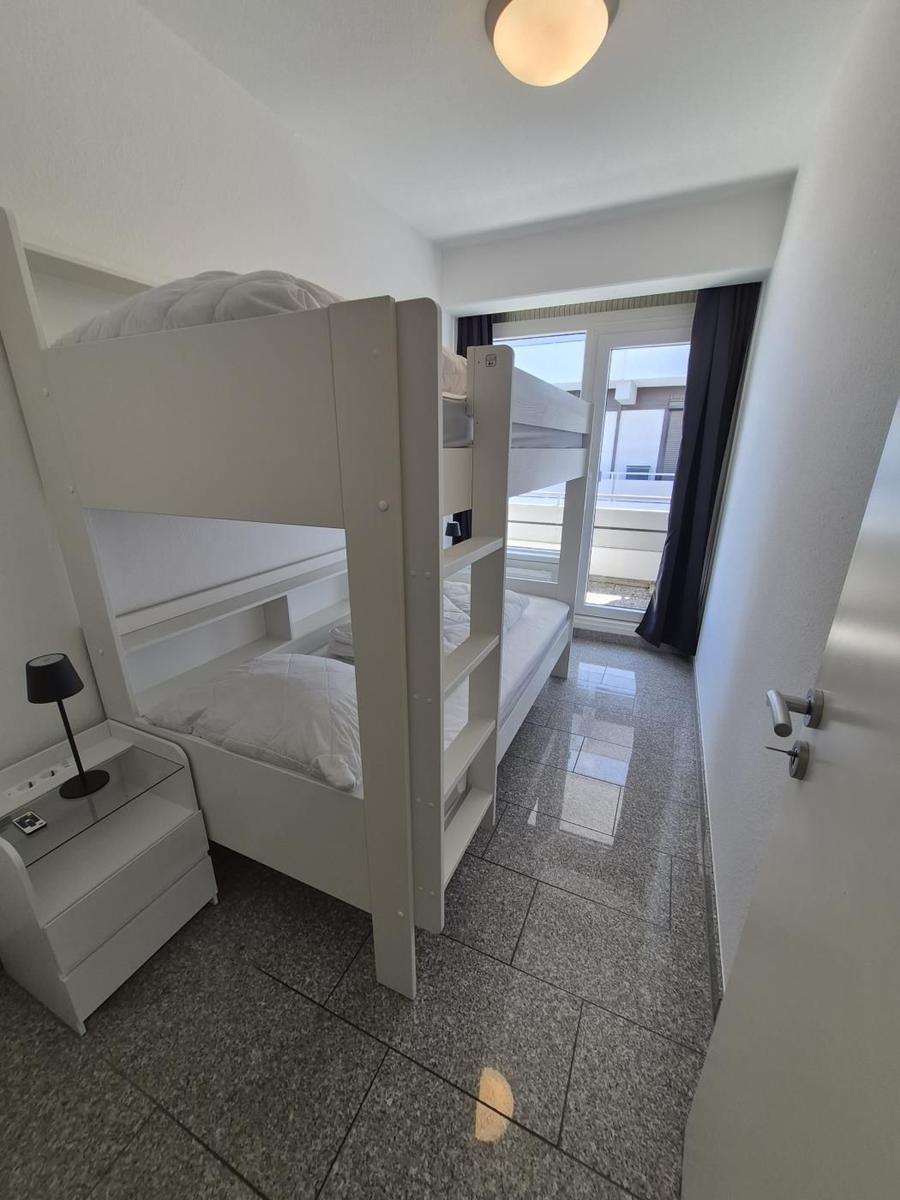 Zimmer mit Doppelstockbett, Nachttisch und Balkontür.
