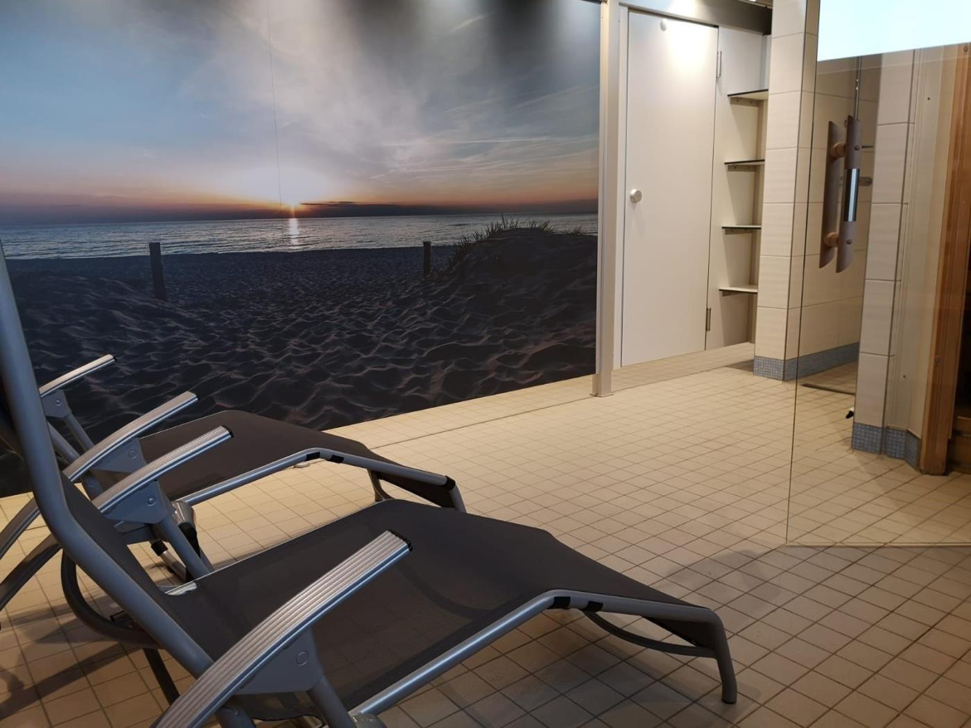 Liegemöbel vor einer Wand mit Strandmotiv, daneben Dusche und Schrank.