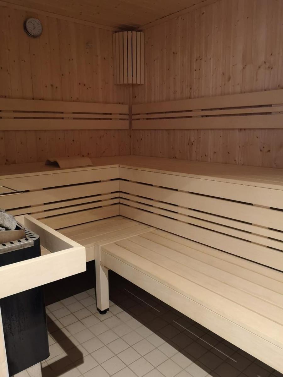 Sauna mit Holzbanken und Bodenfliesen. An der Wand hängt eine Uhr.