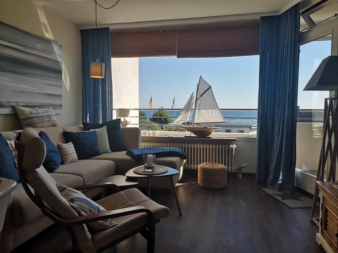 Wohnzimmer mit Meerblick, Sofa, Sessel und Segelschiffmodell auf Balkon.