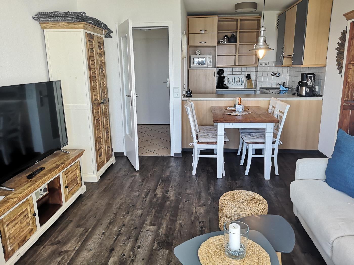 Wohn- und Essbereich mit Küchenzeile, Sofa und Fernseher auf Holzboden.