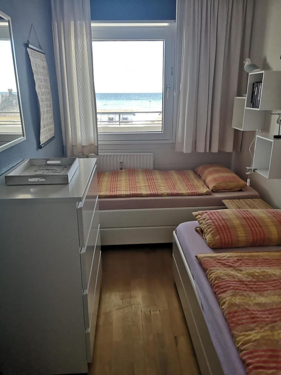 Zimmer mit zwei Betten, Fenster zum Meer und Schrank. Holzboden und Wandregale.