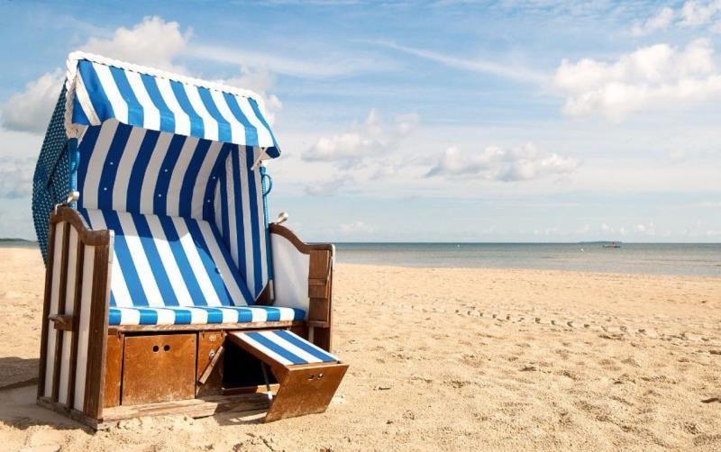 Ein blaues und weißes Strandkörbchen steht auf dem Sand. Der Himmel ist blau mit weißen Wolken.