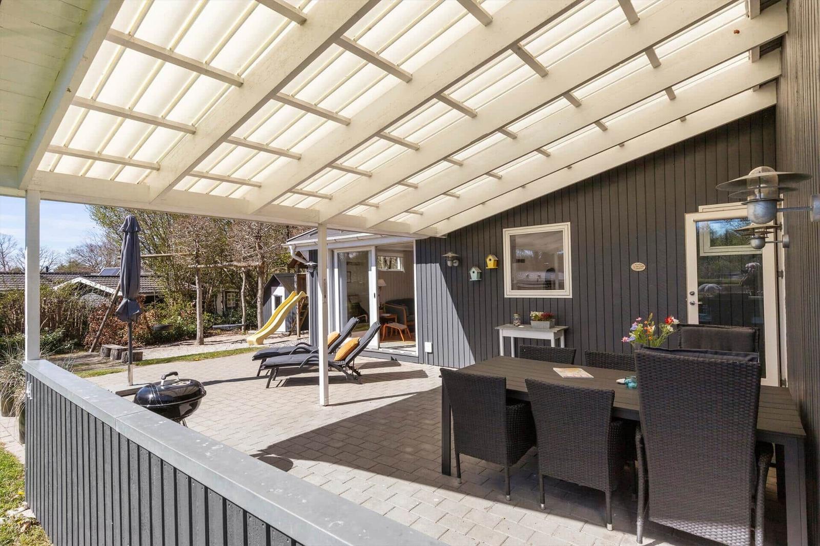Patio with seating, grill, and loungers under roof. View into garden with slide.