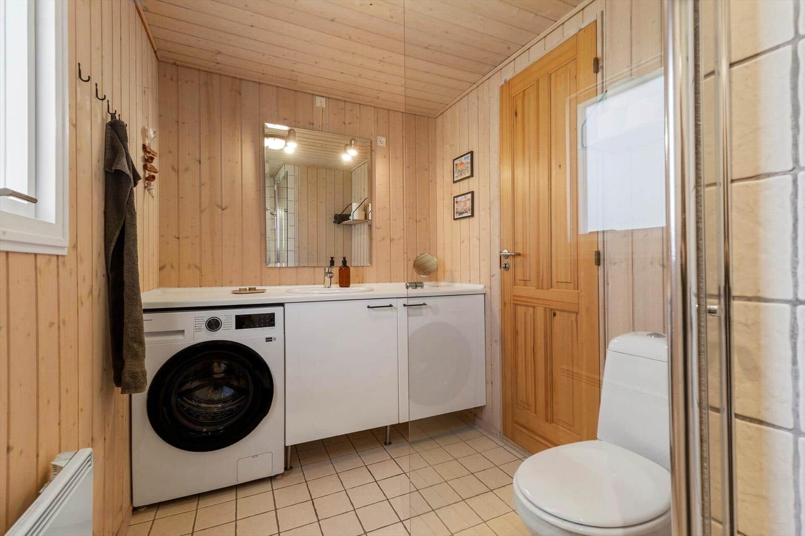 Bathroom with washing machine, toilet, and shower. Wooden walls and tiled floor.