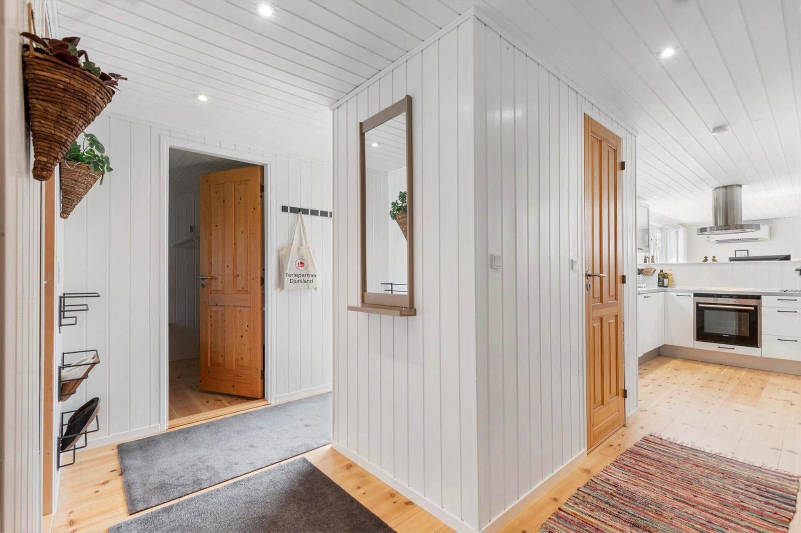House with white walls, wooden doors, and kitchen area. Hanging plants and rugs are visible.