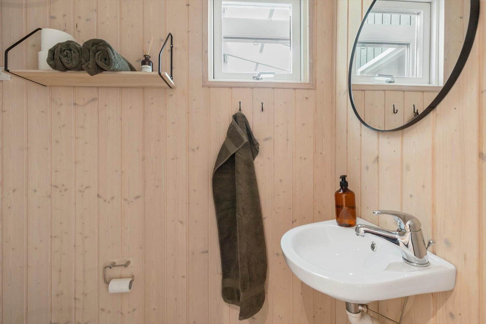 Bathroom with wooden walls, sink, mirror, and towel hooks.