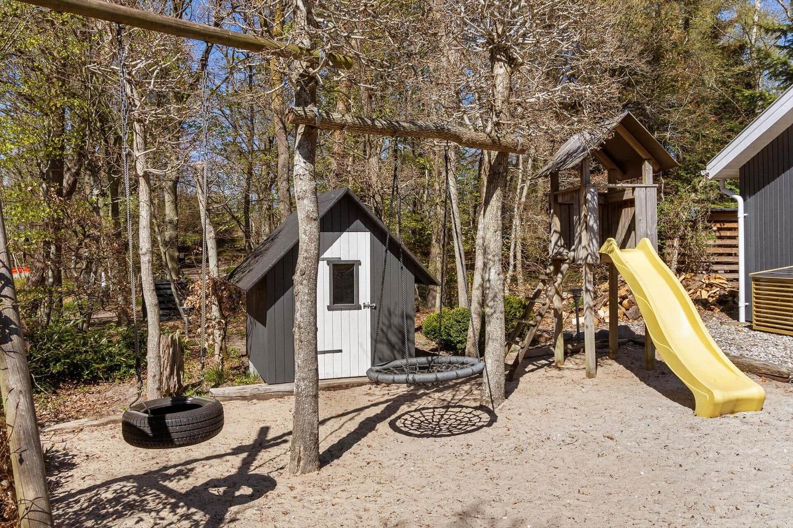 Play area with swing, slide, and playhouse in the woods.