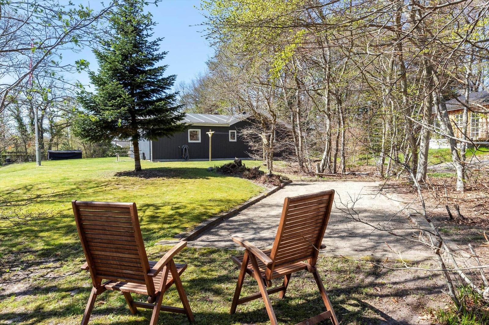 Two wooden chairs sit in the garden facing a house with lawn and trees.