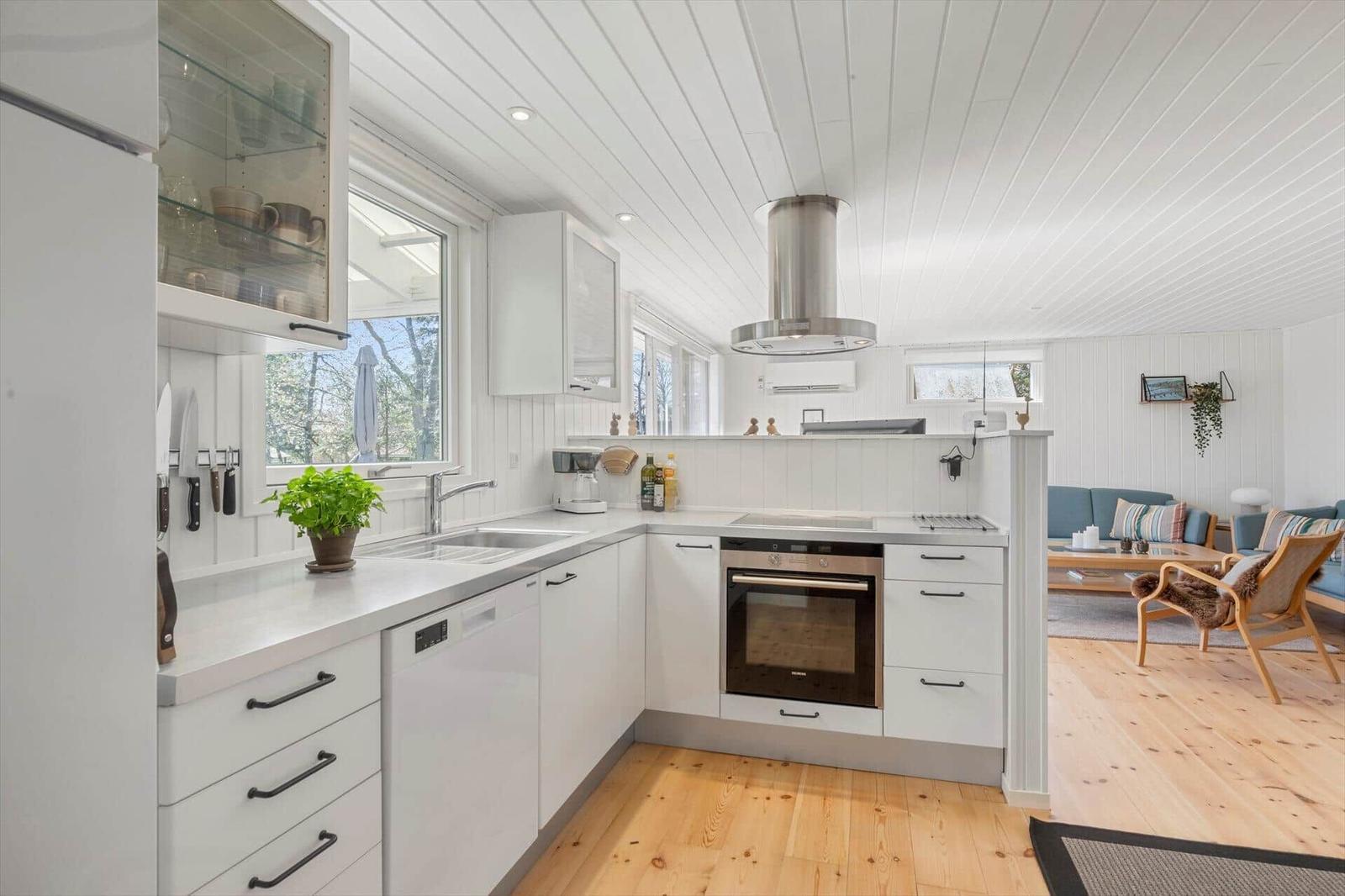 Kitchen with white cabinets, stainless steel oven, and wooden floor. View into the living room.