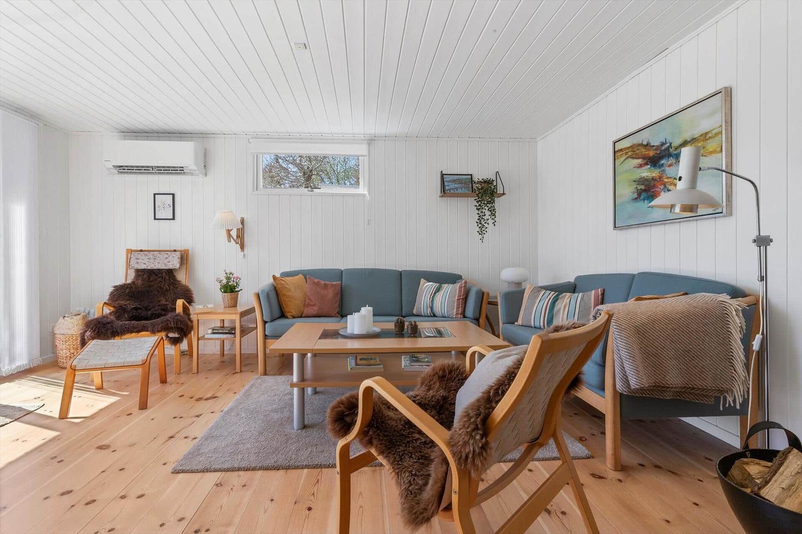 A living room with wooden floor, blue sofas, and wooden furniture. A painting hangs on the wall.
