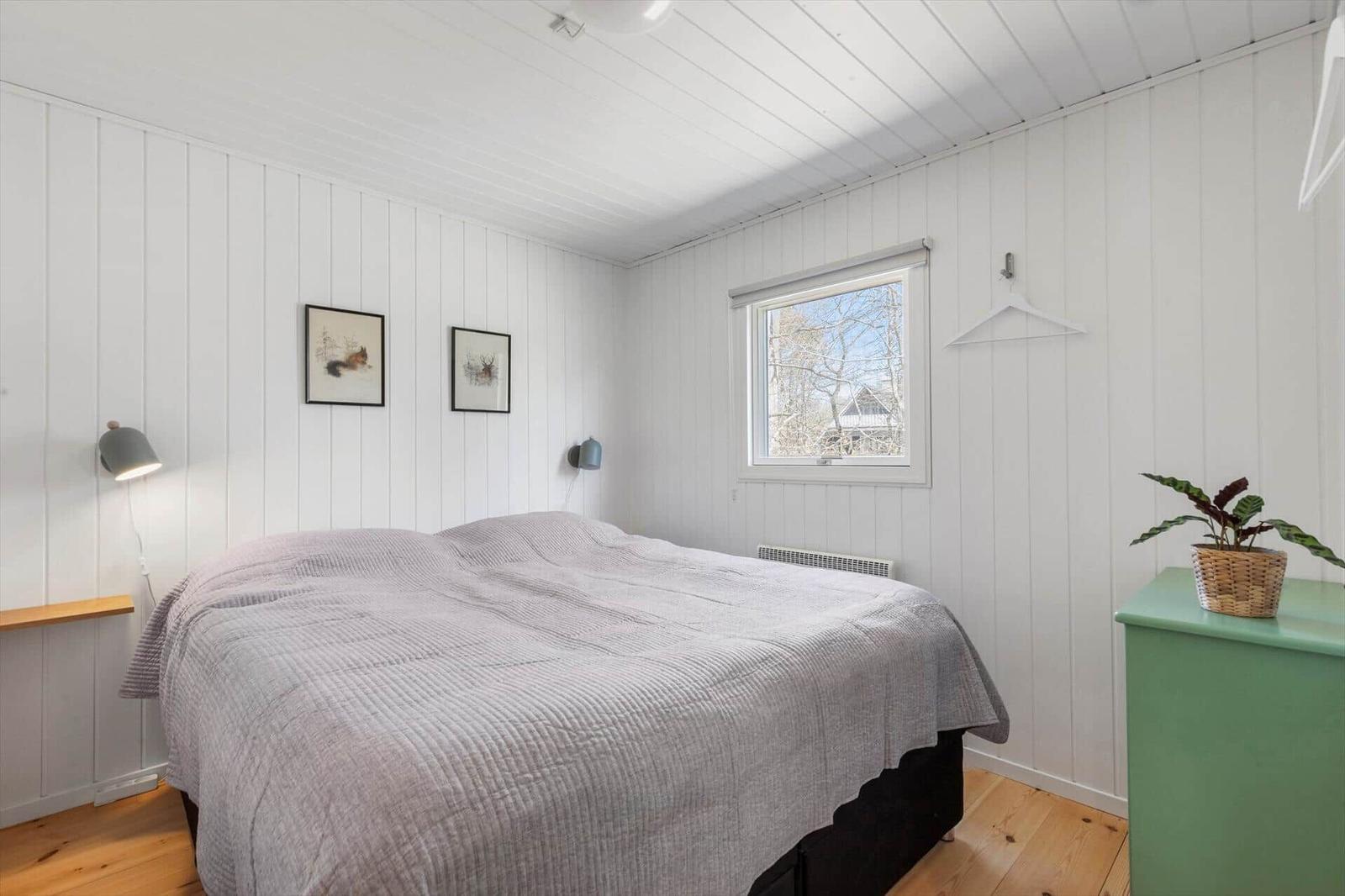Bedroom with bed, window, and green dresser. Walls and ceiling are white paneled.