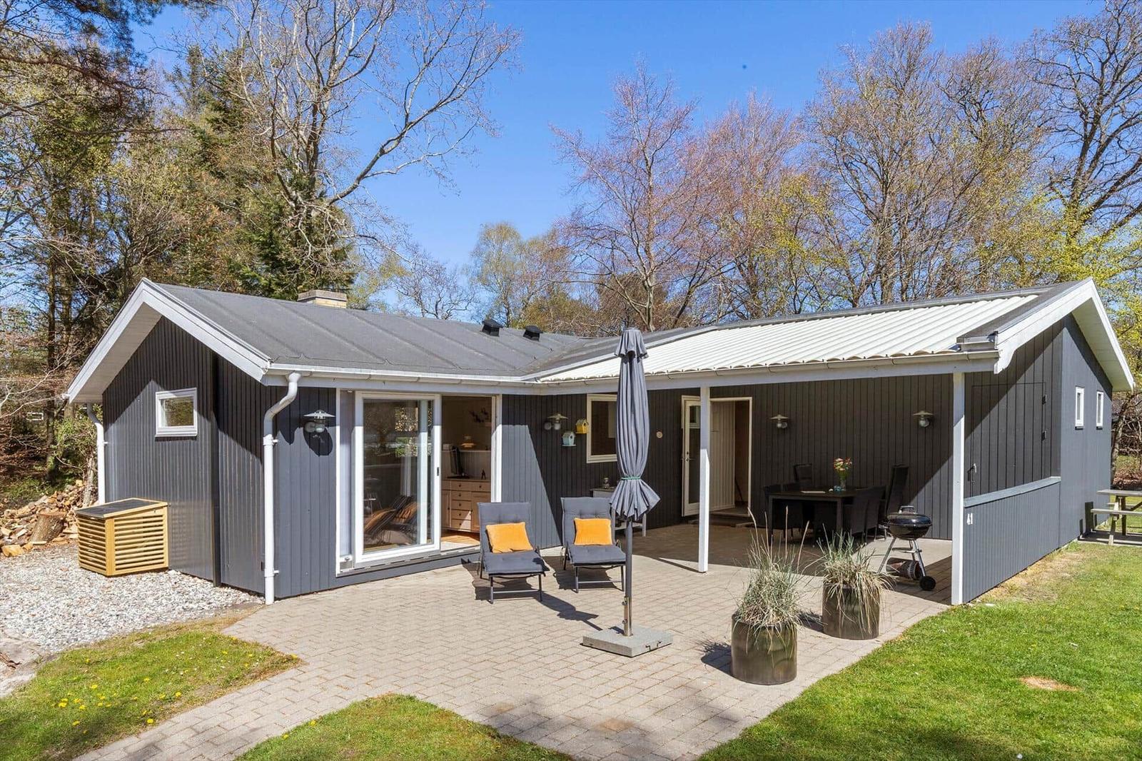 A gray vacation home with terrace, garden, and grill area. Wooden windows and seating are visible.