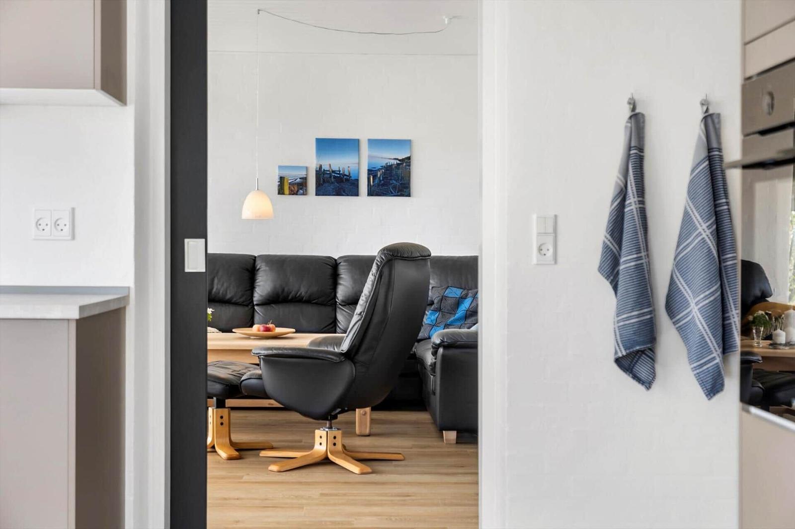 A living room with a black sofa and a chair. Pictures hang on the wall.