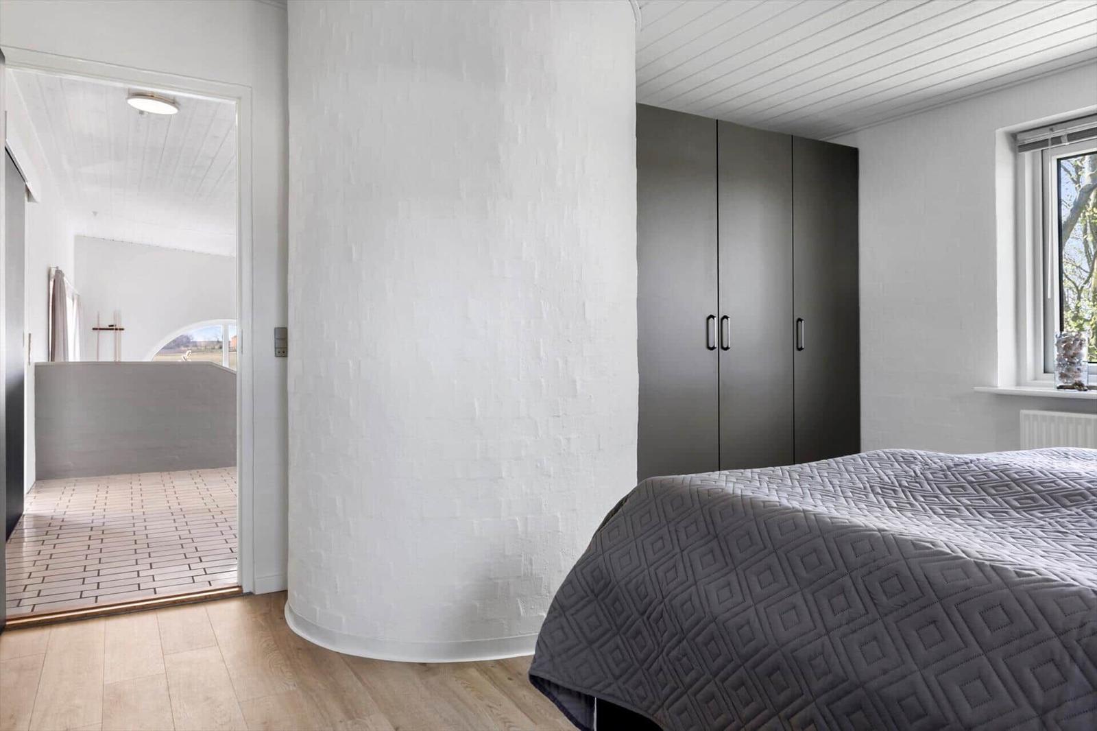 Bedroom with bed, wardrobe, and pillar. Passage to shower with tiled floor.