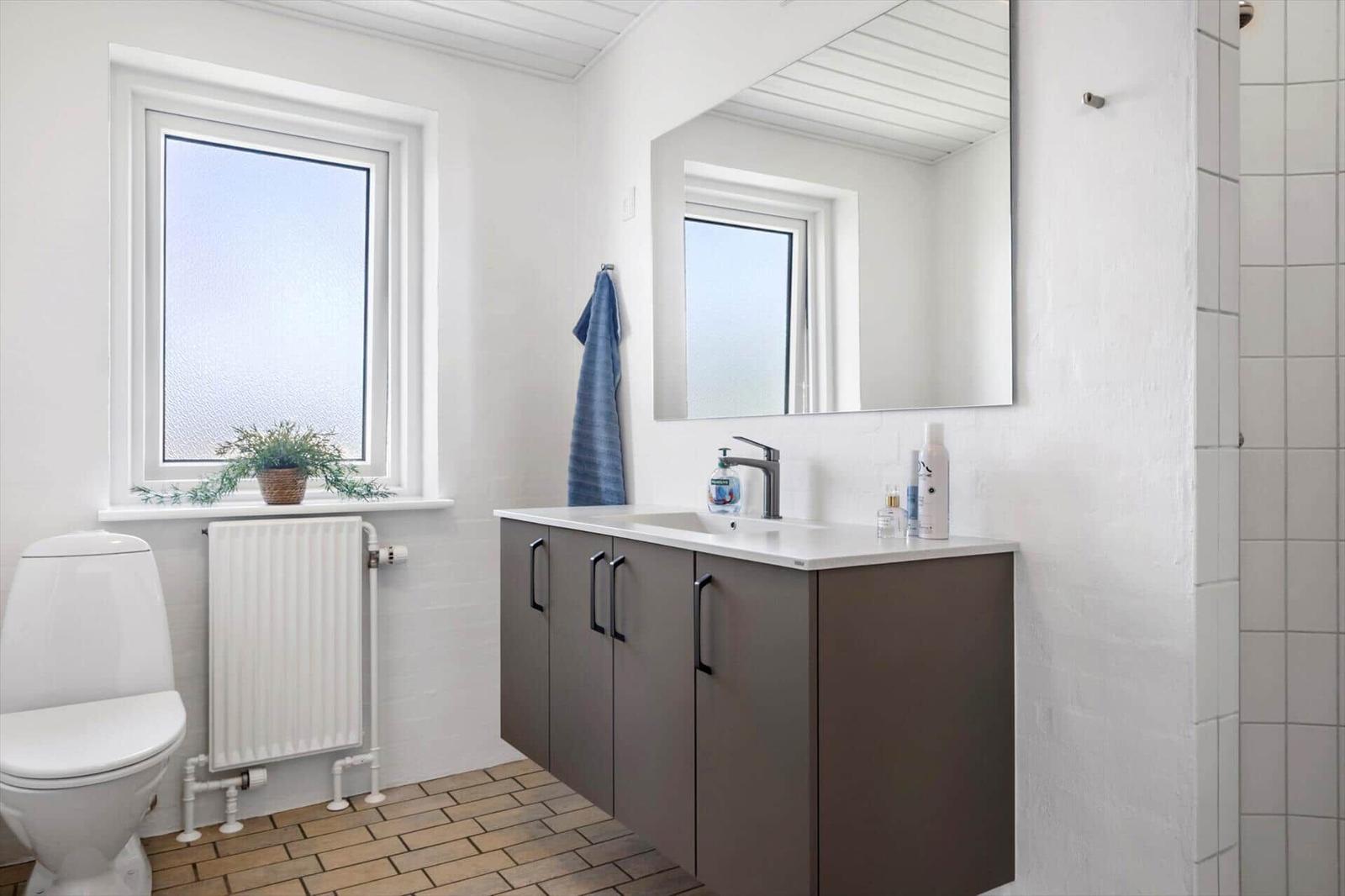 Bathroom with sink, mirror, toilet, and window.