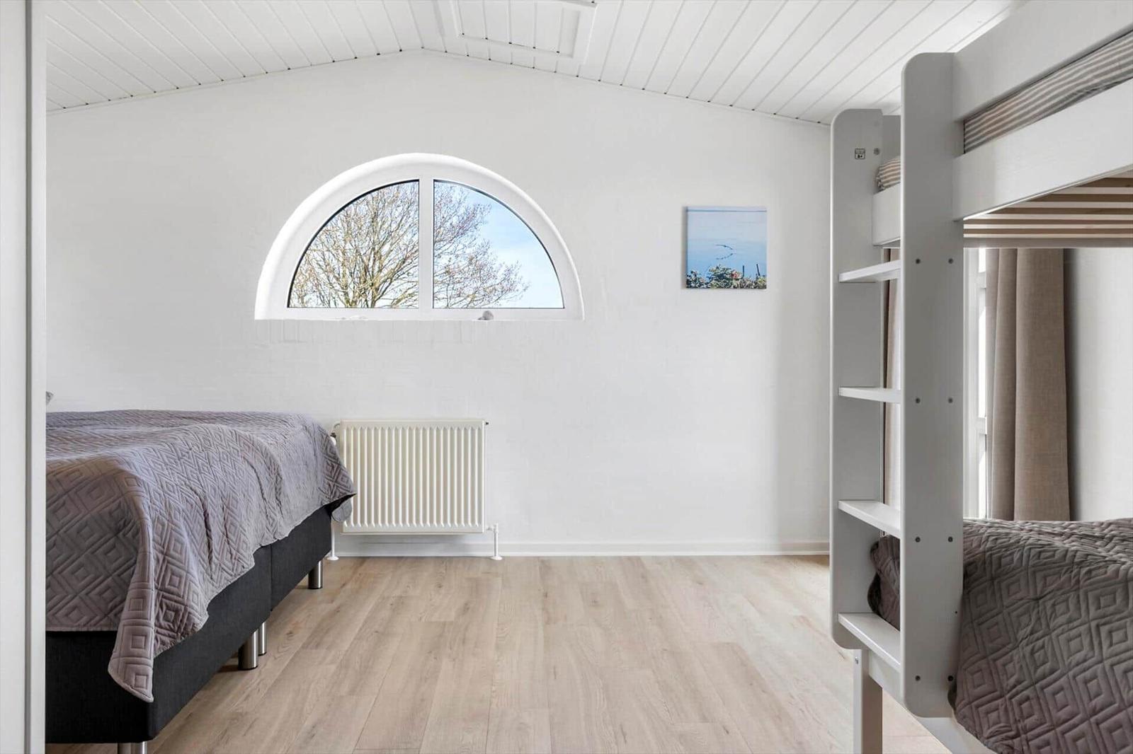 Room with double bed, ladder, and bunk bed. Arched window and wooden floor.
