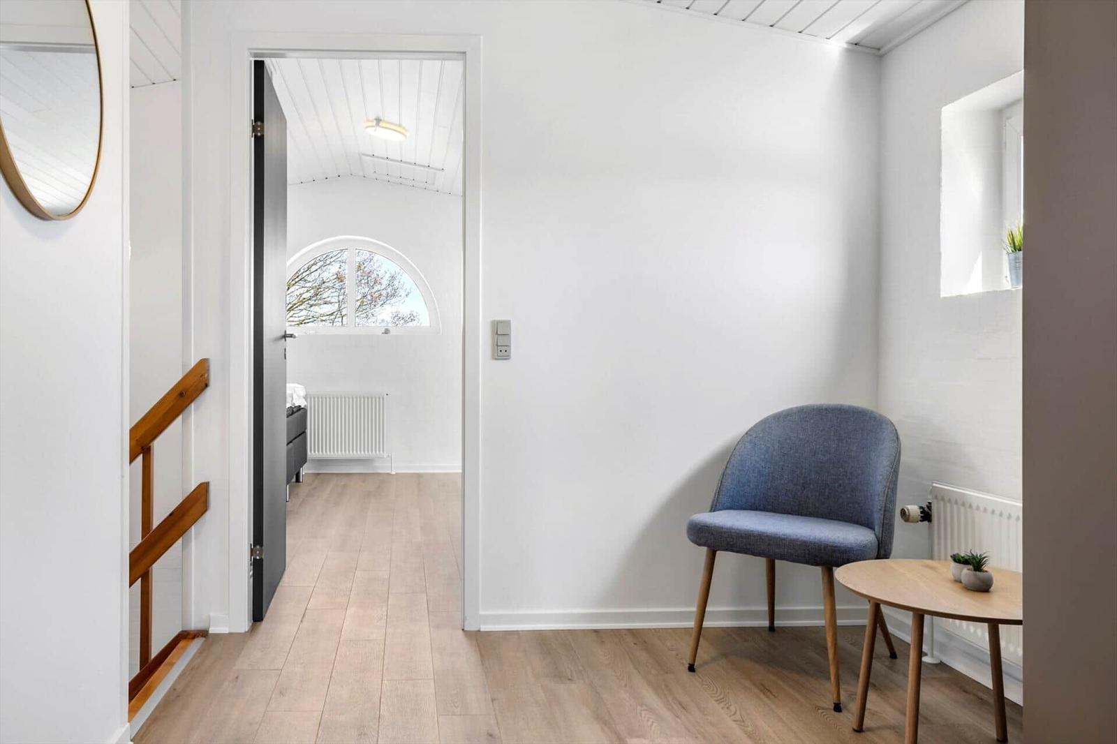 Entrance area with chair and table. Corridor to bedroom with arched window.