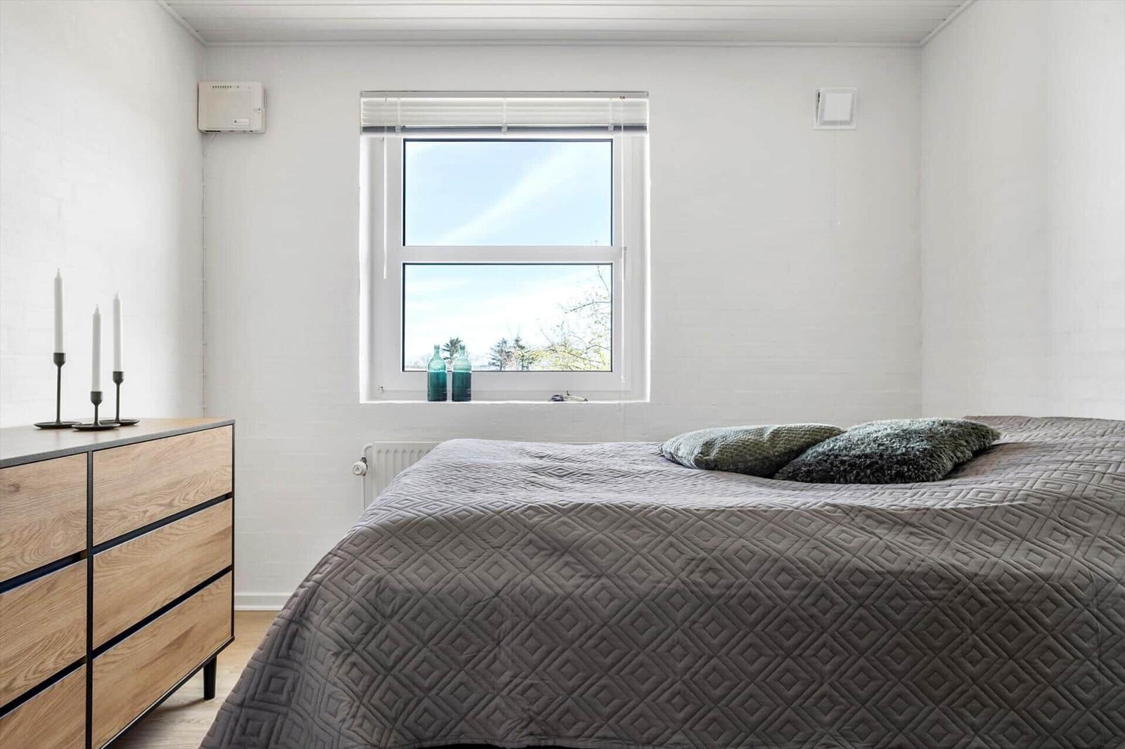 Bedroom with bed, window, and dresser. Two green bottles sit on the windowsill.