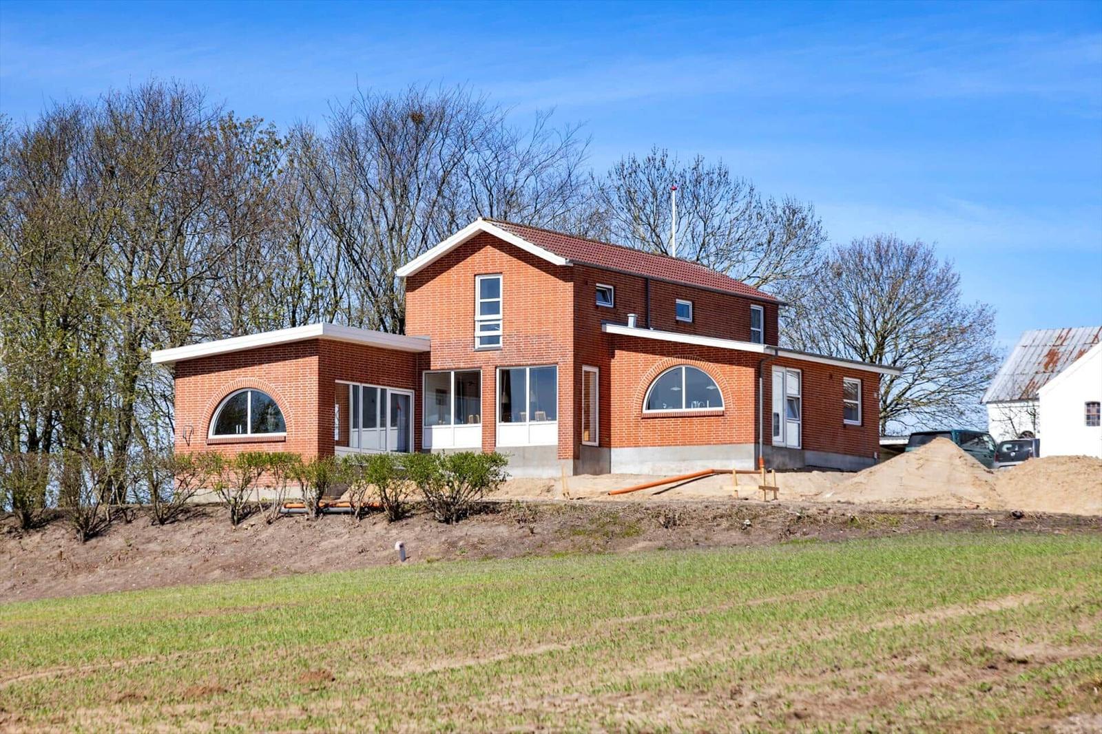 New brick building with large windows and garden. Construction site in background.