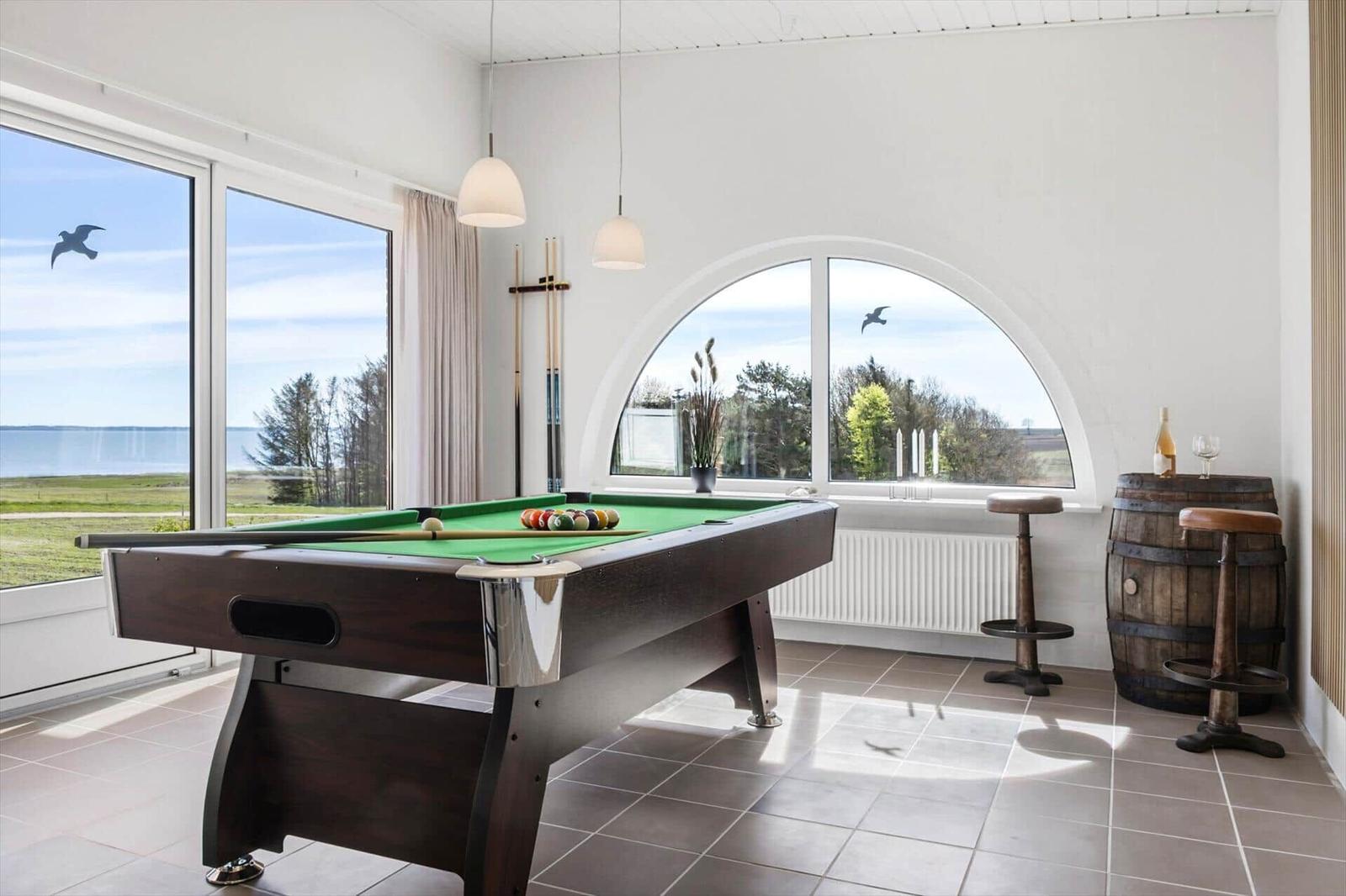 Pool table with green felt and balls. Large windows with view of the landscape.