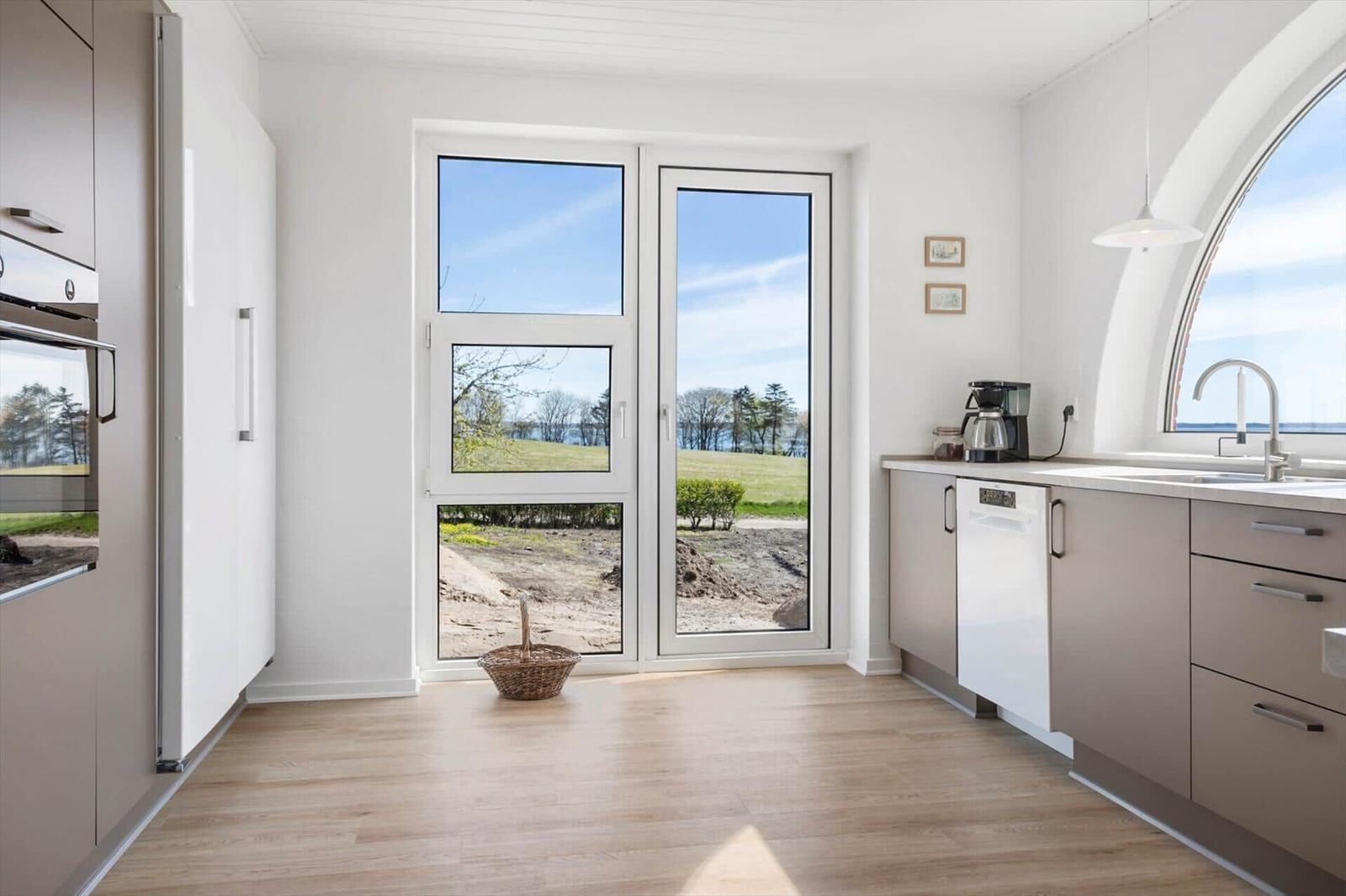 Kitchen with view of green field and water through large windows.