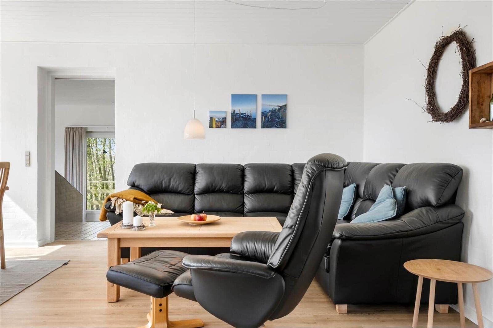 Living room with black leather sofa, wooden table, and chair. Wall has pictures and a wreath.