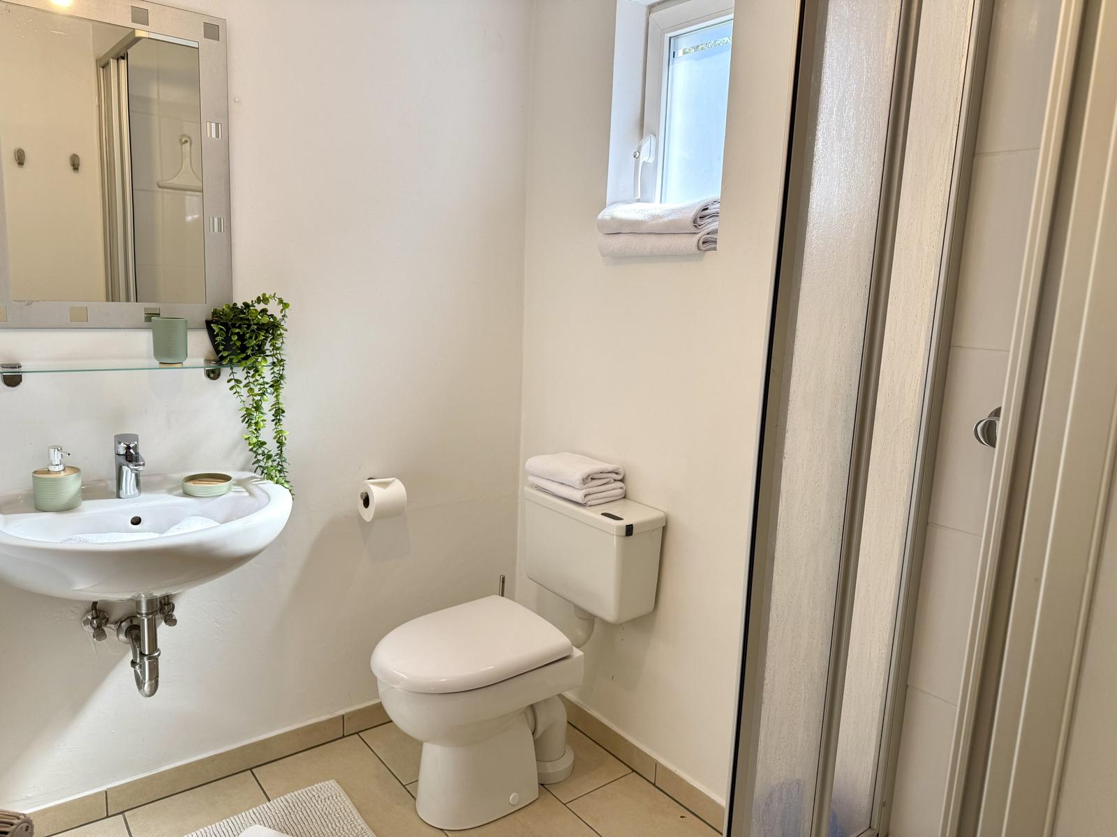 Badezimmer mit Toilette, Waschbecken und Dusche. Fenster mit Handtüchern.