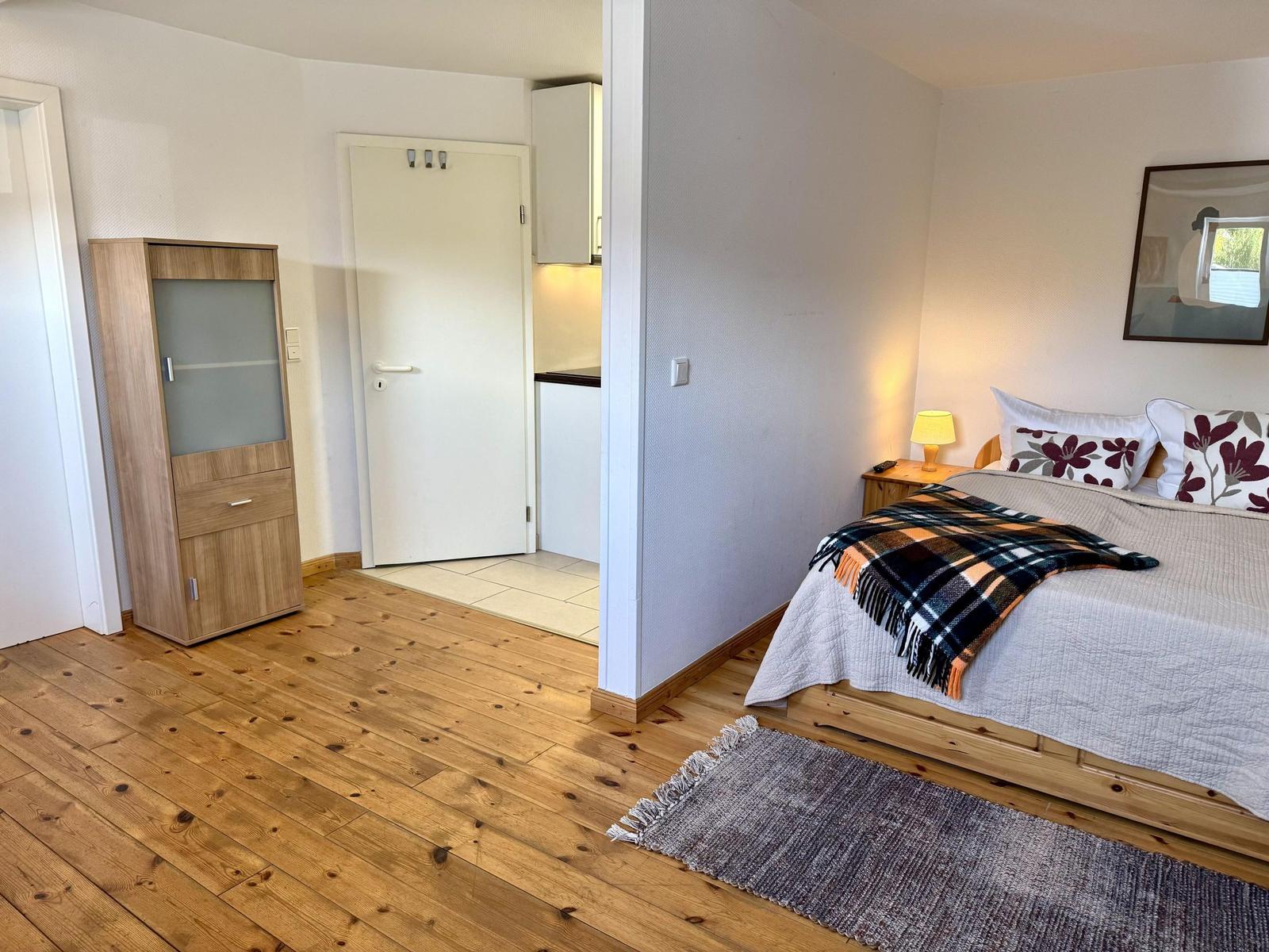 Schlafzimmer mit Bett, Nachttisch, Lampe und Kleiderschrank. Holzfußboden und Teppich.