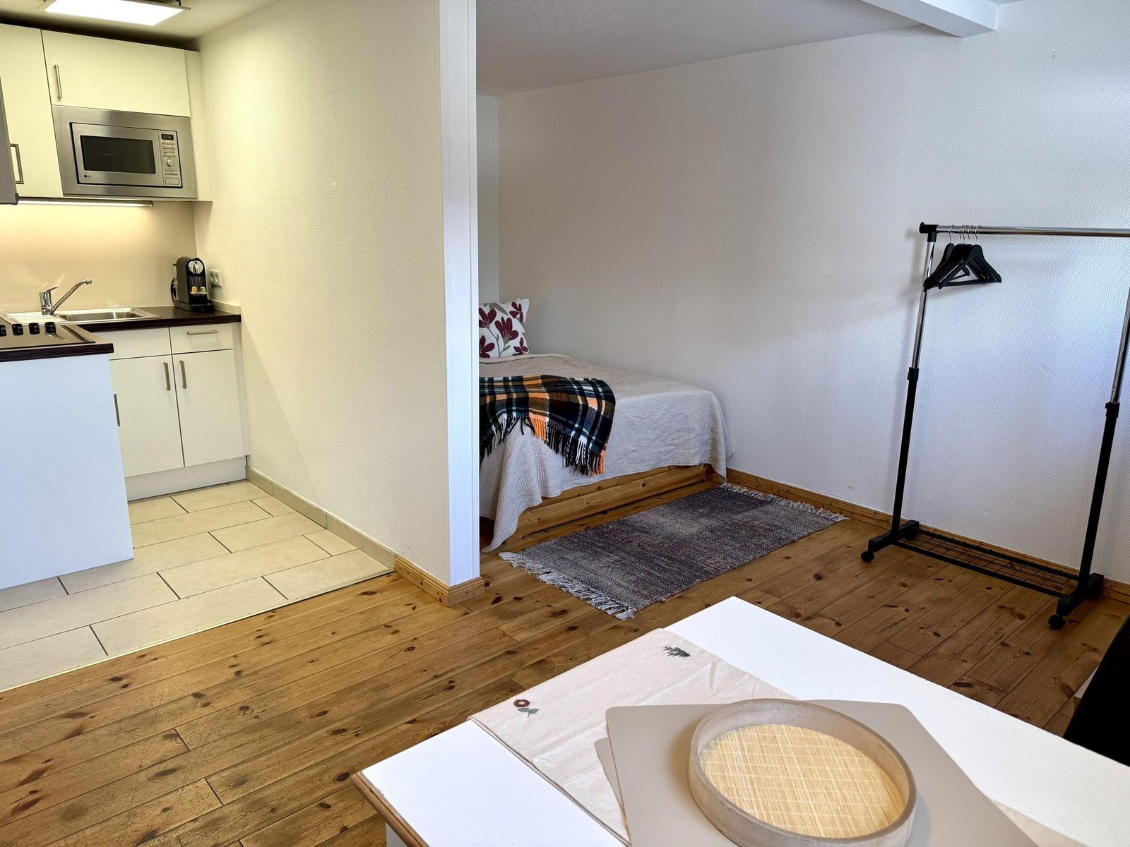 Küche mit Mikrowelle und Schlafzimmer mit Bett und Kleiderständer.