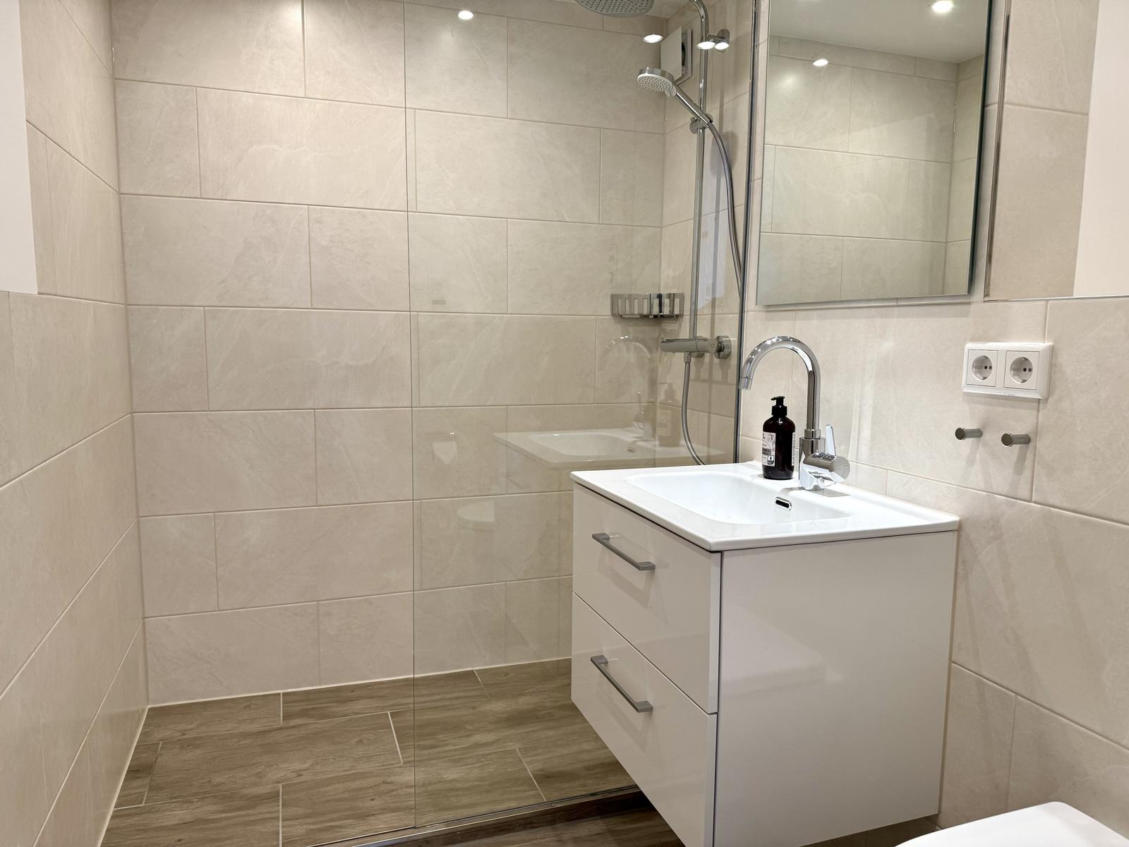 Moderne Dusche mit Glaswand, Waschbecken und Spiegel an der Wand.