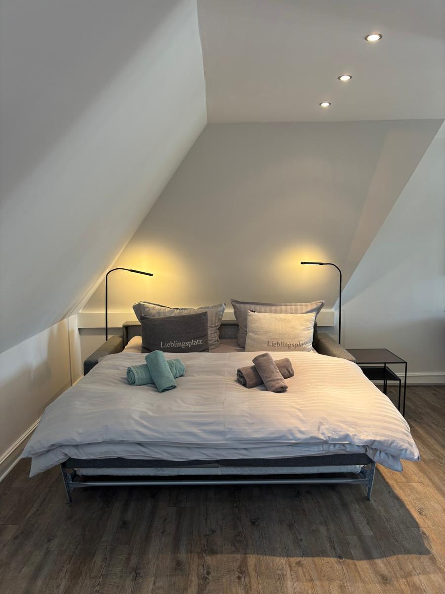 Schlafzimmer mit Doppelbett, zwei Stehlampen und Holzboden unter schrägen Wänden.