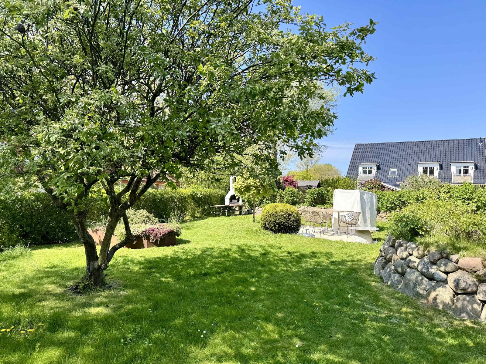 Garten mit Baum, Grill und Sitzgruppe vor einem Haus.