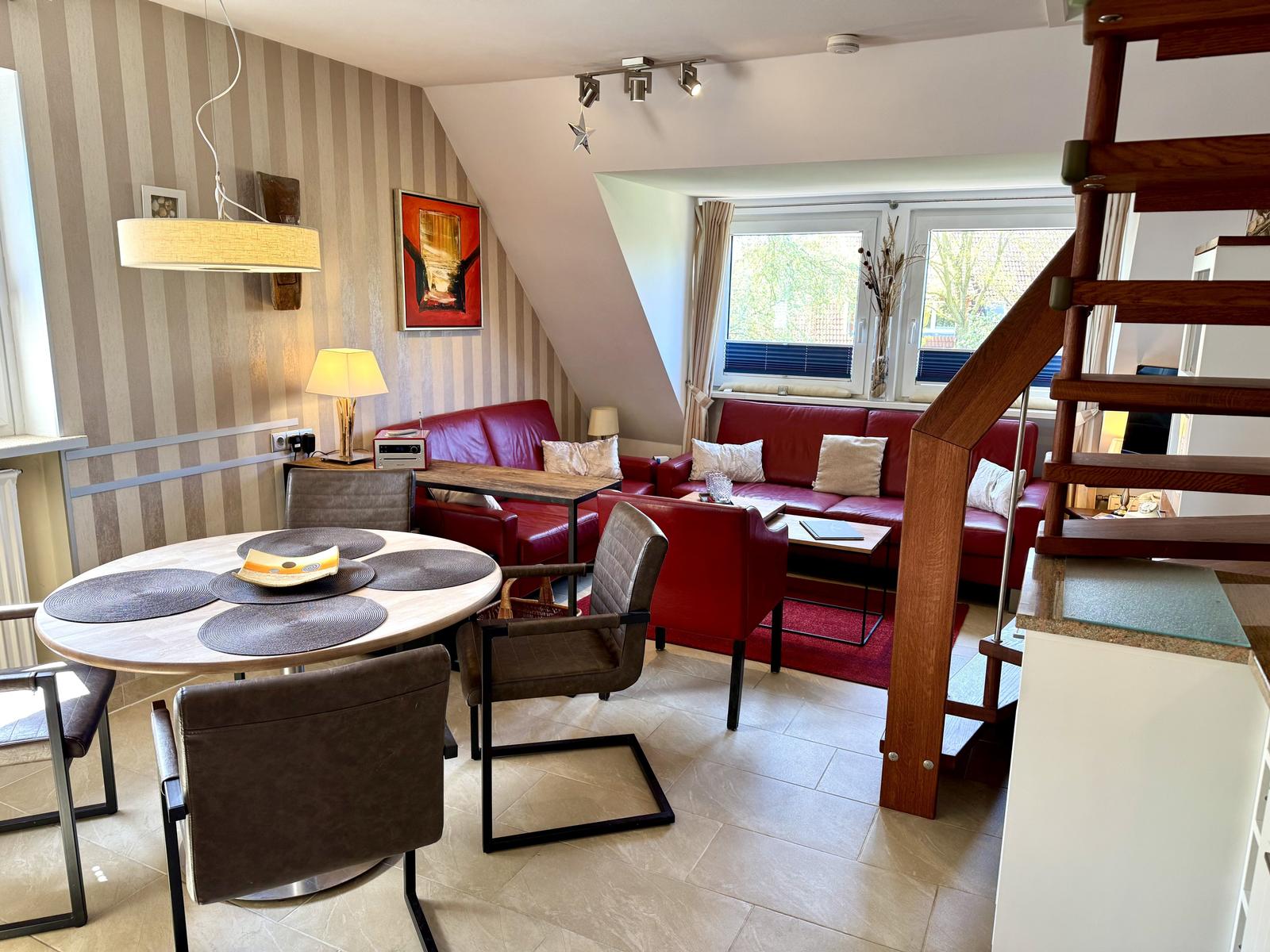 Wohn- und Essbereich mit rotem Sofa, runden Tisch und Holztreppe.