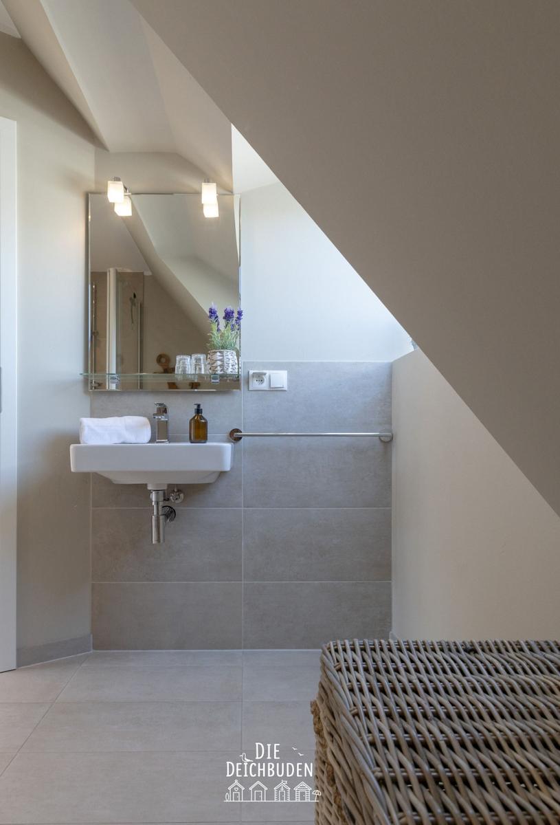 Badezimmer mit Waschbecken, Spiegel und Duschbereich unter Dachschrägen.