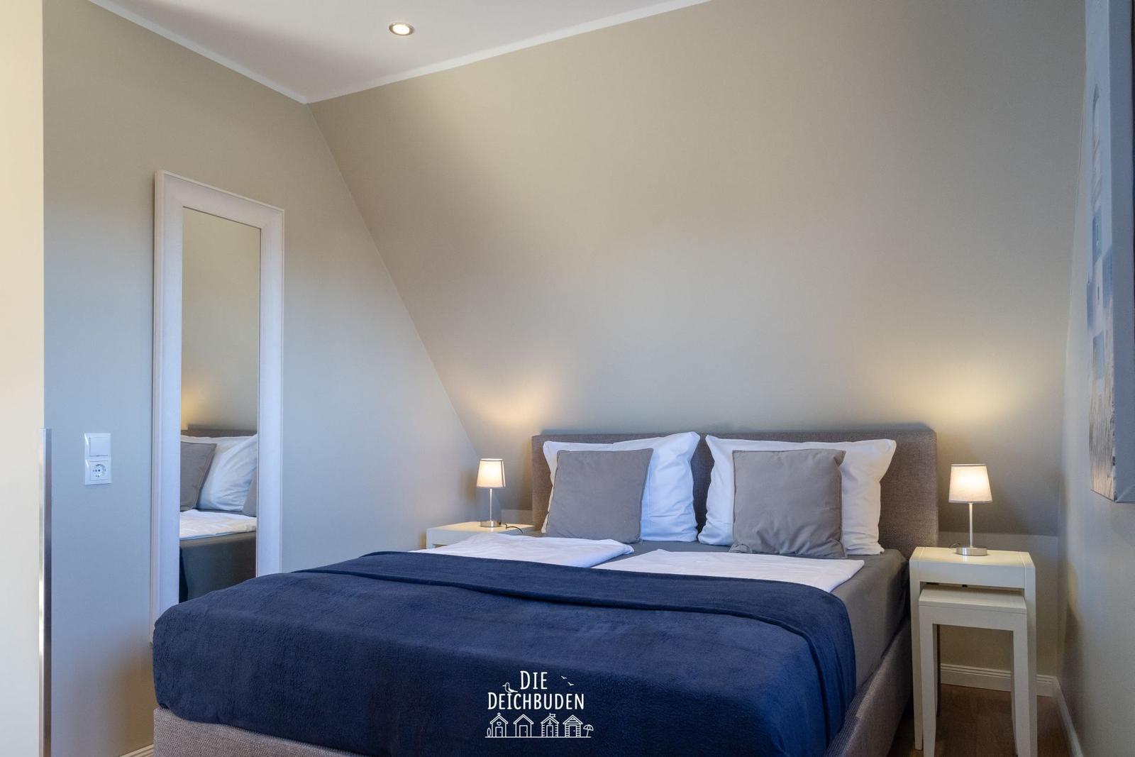 Schlafzimmer mit Doppelbett, zwei Nachttischen und Spiegel an der Wand.