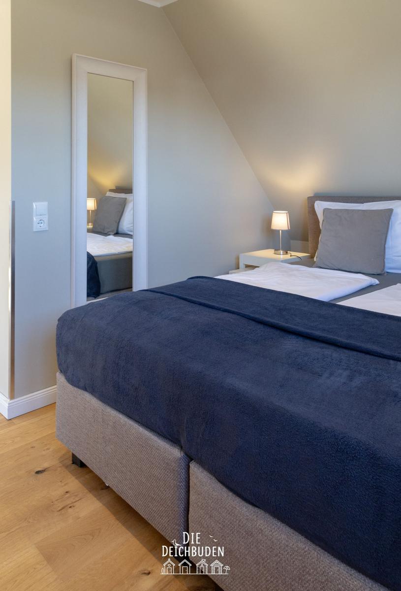 Schlafzimmer mit Doppelbett, Nachttisch und Spiegel an der Wand.