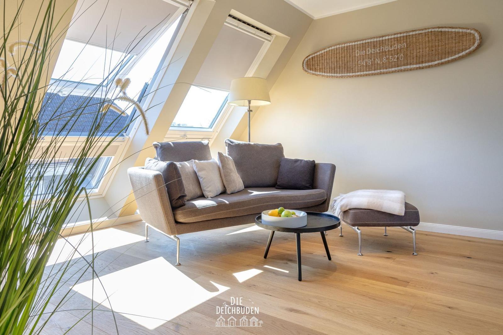 Wohnzimmer mit Sofa, Couchtisch und Fenster. Wanddekoration und Pflanze sichtbar.