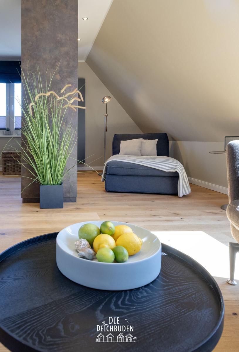 Schlafzimmer mit Dachschräge, Bett, Stehlampe und Pflanze. Tisch mit Früchten im Vordergrund.