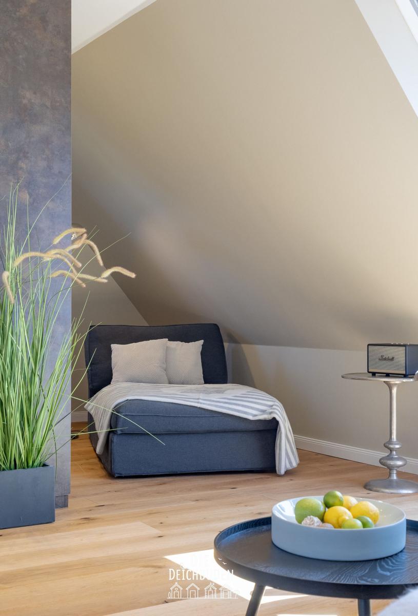 Schlafzimmer mit Dachschrägen, blauem Sofa, Holzboden und Pflanze.