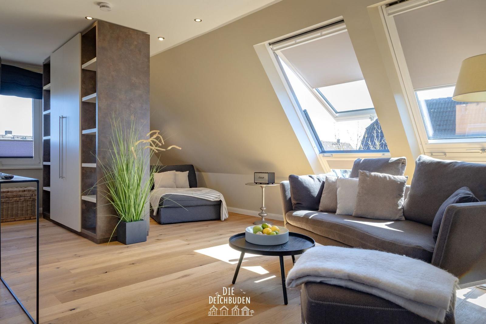 Wohnbereich mit Sofa, Sitzbank und Dachfenstern. Holzboden und eingebaute Regale.
