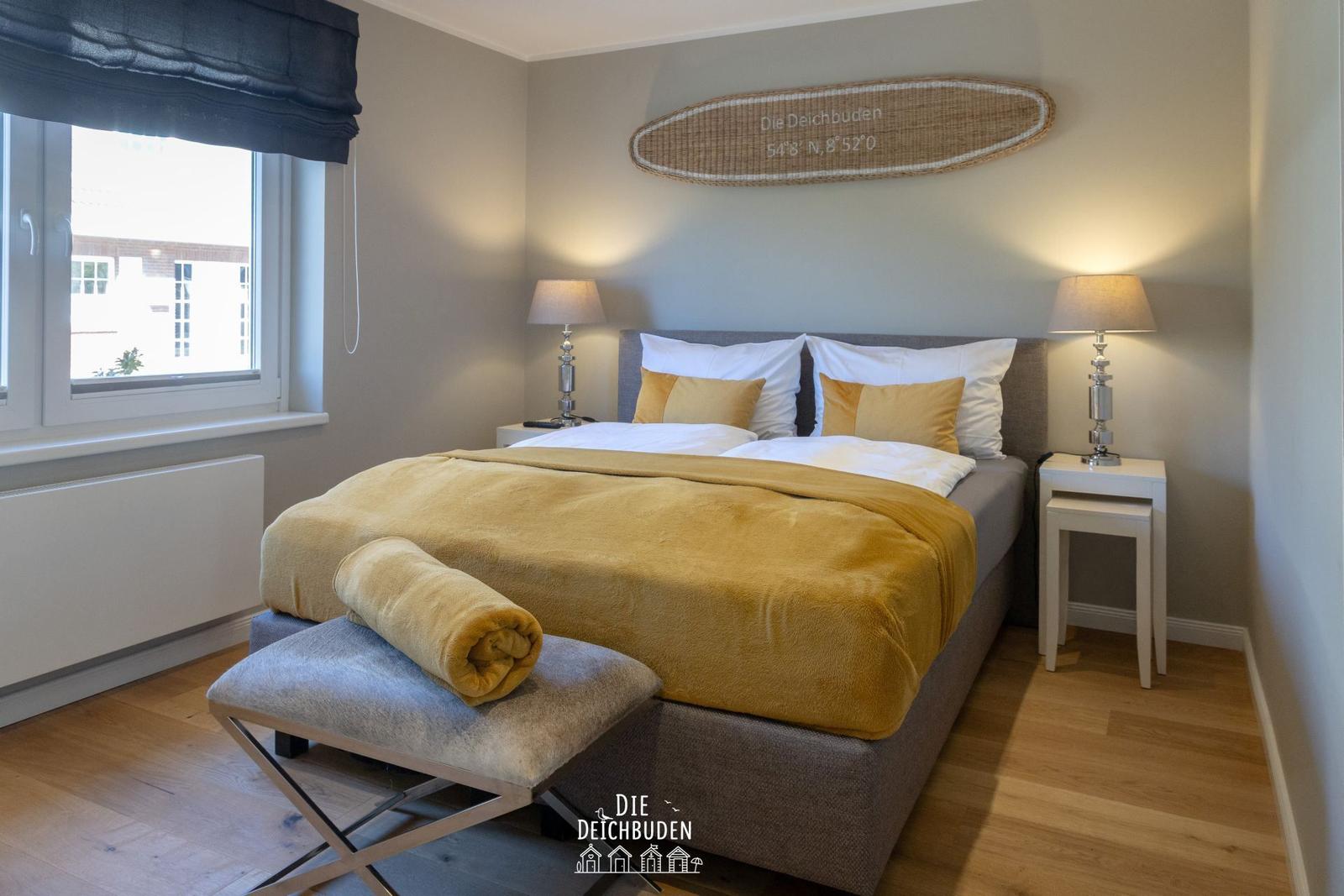 Schlafzimmer mit Bett, Nachttischen und Fenster. Wanddekoration mit Koordinaten.