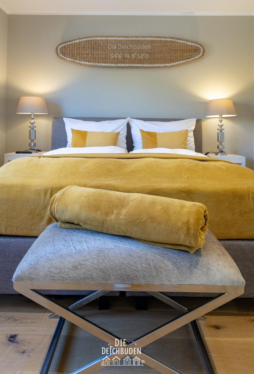 Schlafzimmer mit Bett, Kissen und Decke. Holzfußboden und Wanddekoration.